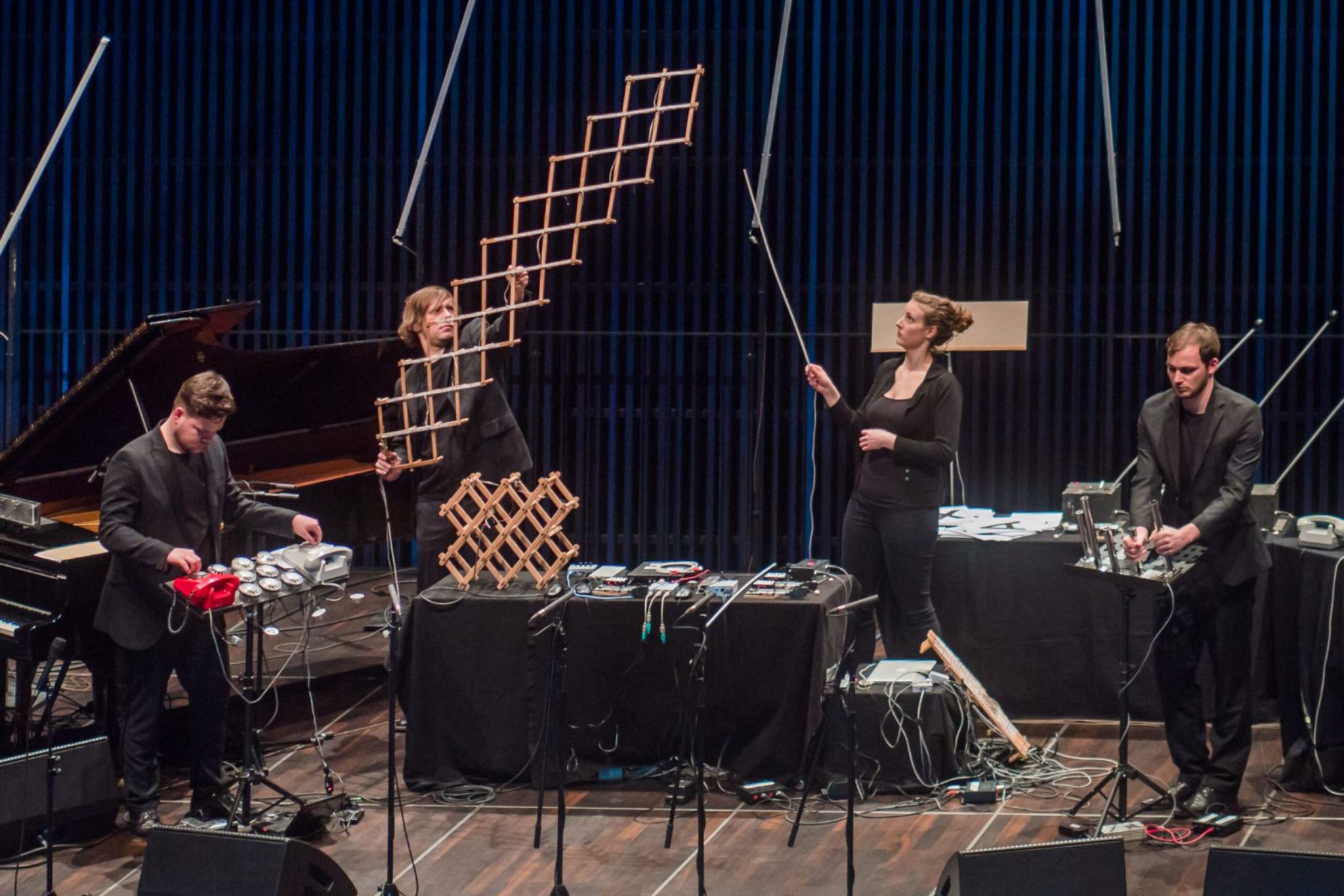 Vier Musiker:innen des Ensembles Atonor auf der Bühne, umgeben von ungewöhnlichen Klanginstrumenten und Kabeln, während sie eine experimentelle Performance mit Objekten und elektronischen Geräten präsentieren.