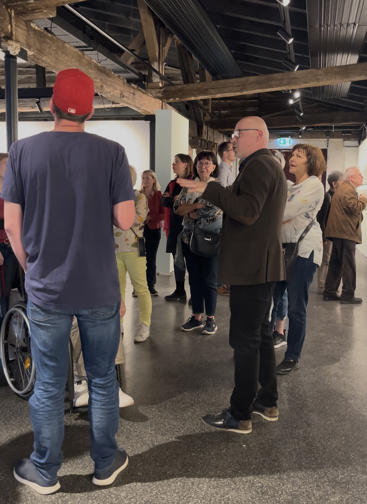 Besucherinnen und Besucher in einer Führung durch die Ausstellung „Nach den Maschinen 2025“ im Inneren des Salinemuseums Halle. Im Vordergrund erläutert ein Mann in schwarzem Sakko Details zur Industriefotografie, während die Gruppe aufmerksam zuhört.